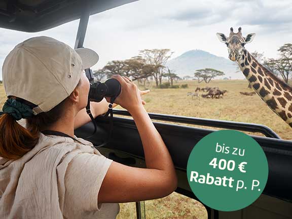 Frau im Safarijeep sieht eine Giraffe