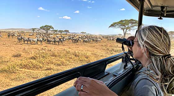 Frau im Safari-Jeep schaut durch ein Fernglas
