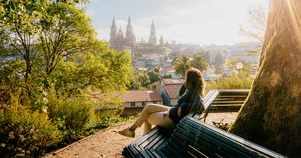 Frau sitzt im Park auf einer Bank und schaut auf Santiago de Compostela mit der Kathedrale.