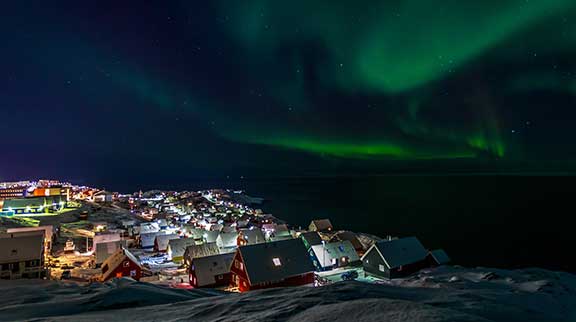Nachtaufnahme der Stadt Nuuk mit Polarlichtern am Himmel.
