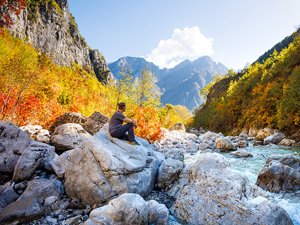 Mann sitzt auf Stein und schaut auf die Alpen.