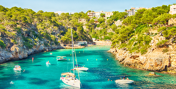 Boote vor einer spanischen Bucht mit türkisblauem Wasser.