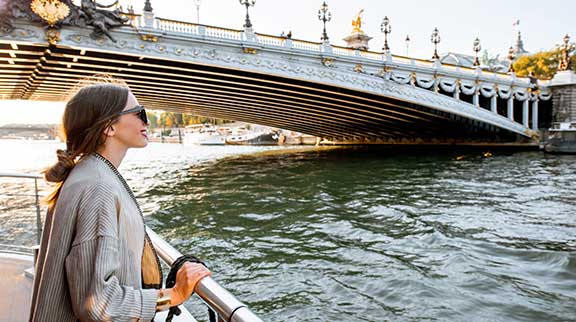 Frau schaut von Flusskreuzfahrtschiff auf vorbeiziehende Stadt.