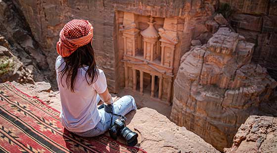 Frau blickt von einem Felsen auf die Felsenstadt Petra runter.