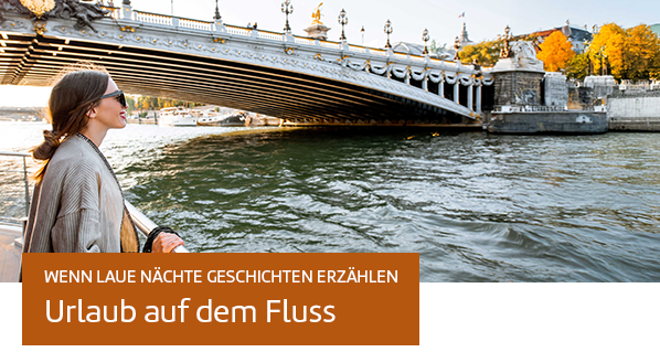 Frau steht an der Reeling eines Flusskreuzfahrtschiffes und schaut auf eine Stadt. Text: Wenn laue Nächte Geschichten erzählen - Urlaub auf dem Fluss.