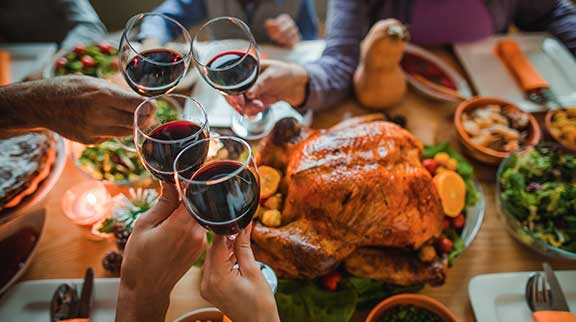 Weingläser stoßen zusammen an, über einem Tisch mit Essen, u. a. ein Truthahn.