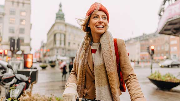 Frau mit orangener Mütze und Schal in einer Stadt im Herbst.