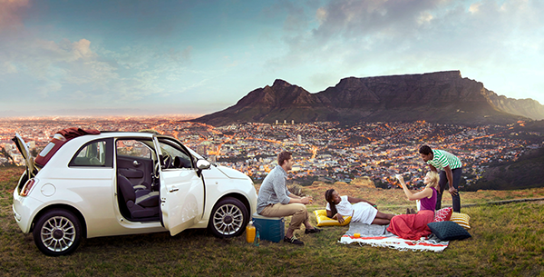Vier Menschen machen ein Picknick neben Ihrem weißen Auto mit Blick auf Kapstadt und den Tafelberg.