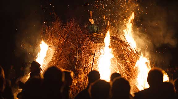 Lagerfeuer bei Nacht mit einer Figur auf dem Lagerfeuer.