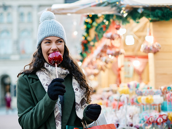 Frau isst roten kandierten Aprfel auf Weihnachtsmarkt.