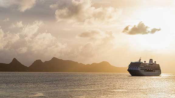 Kreuzfahrtschiff fährt auf hoher See. Im Hintergrund ist Land mit Bergen.