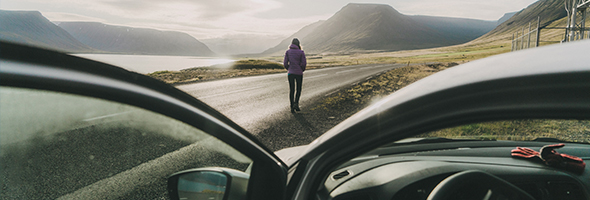Frau blickt auf die Landschaft Islands. Im Vordergrund ist ein Auto zu sehen.